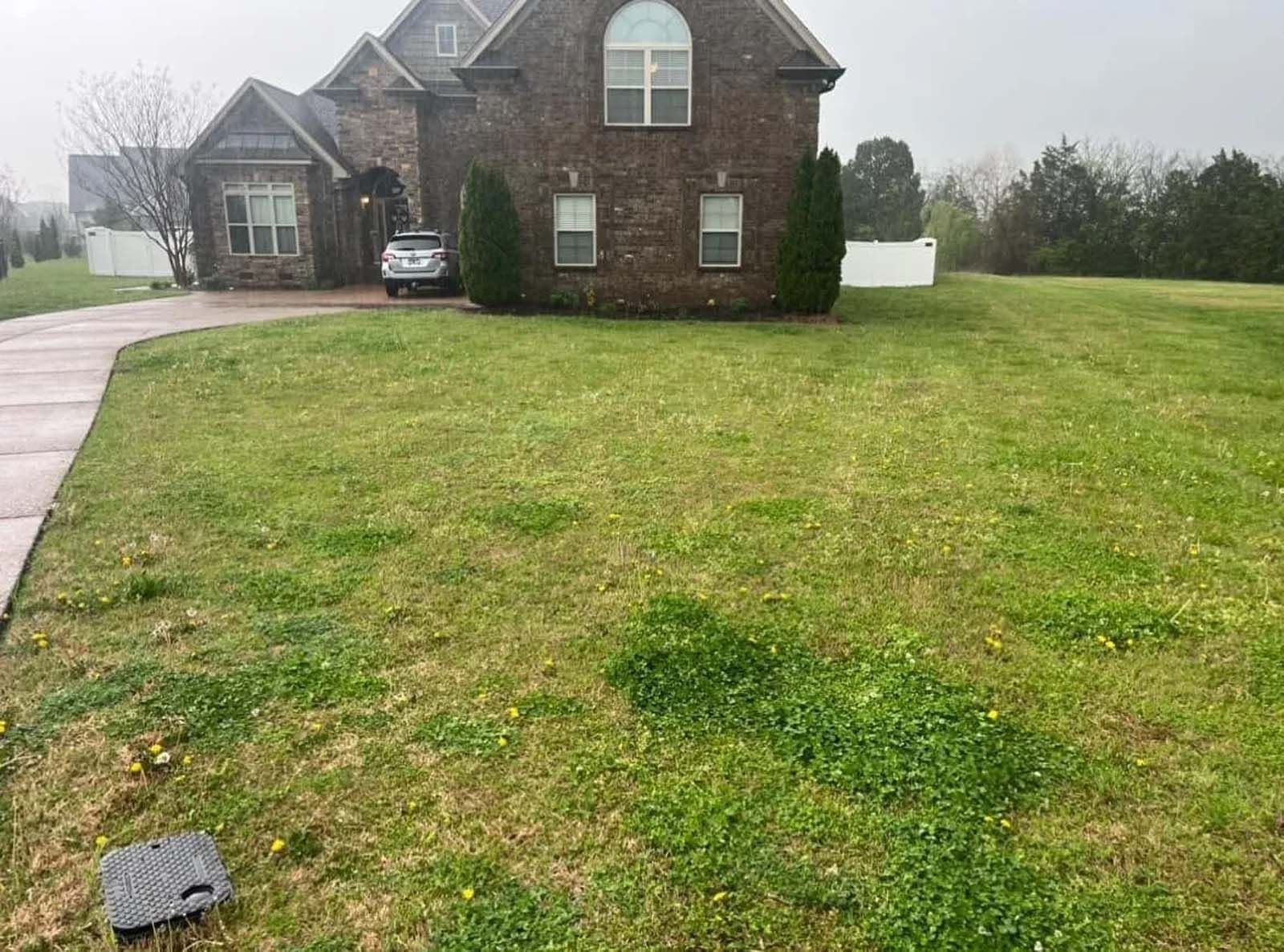 Suburban brick house with a large front lawn and a driveway on a foggy day