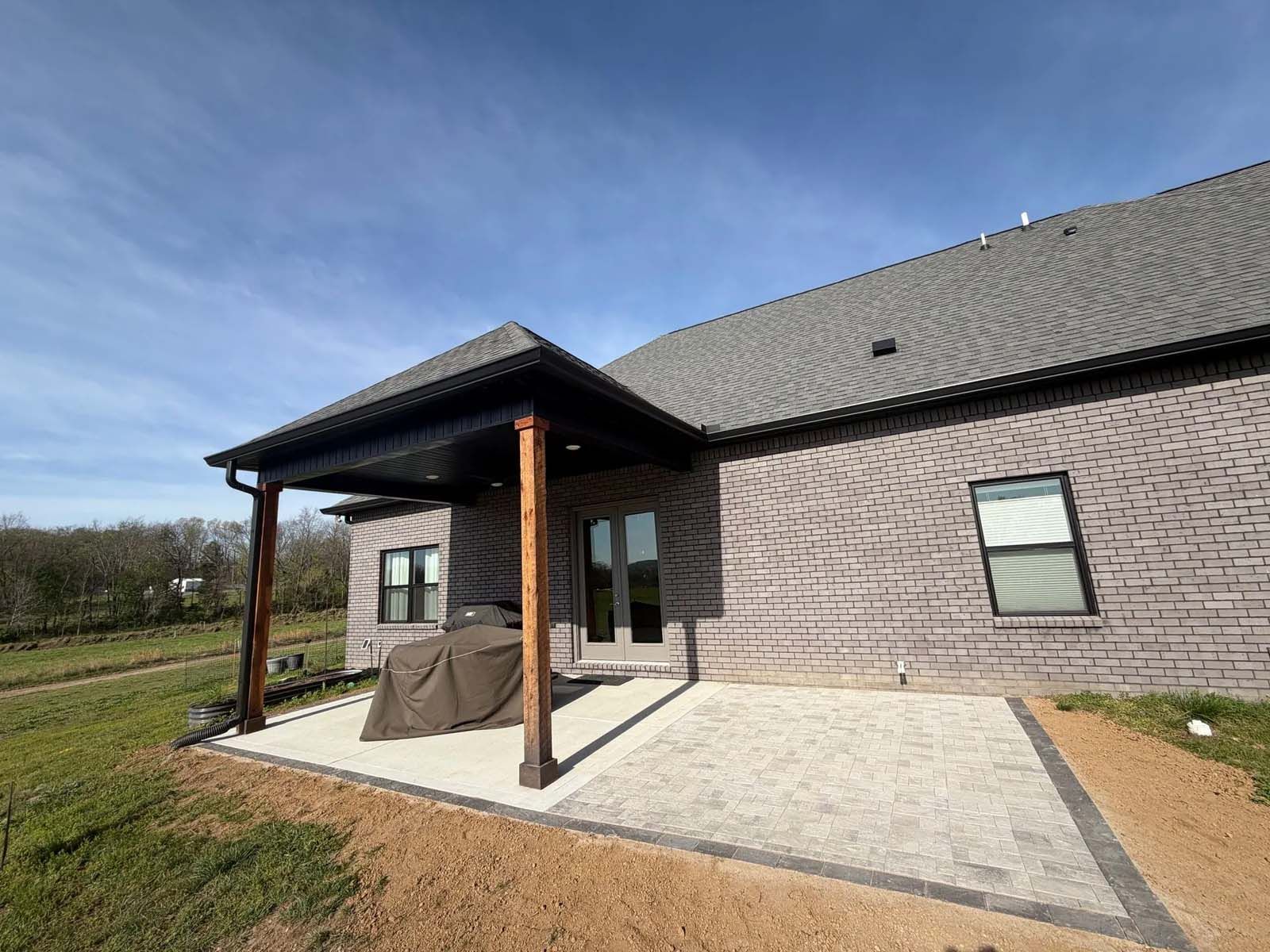 Back patio with covered porch beside a brick house, concrete patio, and lawn under a blue sky
