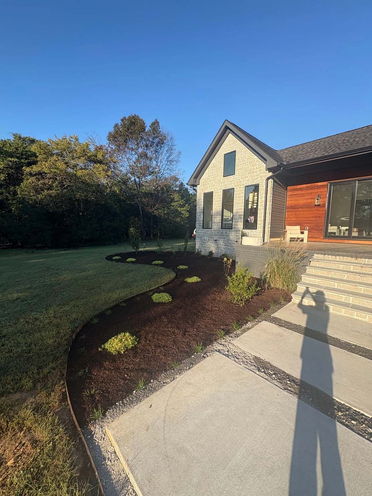 House exterior with curved garden bed, green lawn, and concrete walkway in sunlight