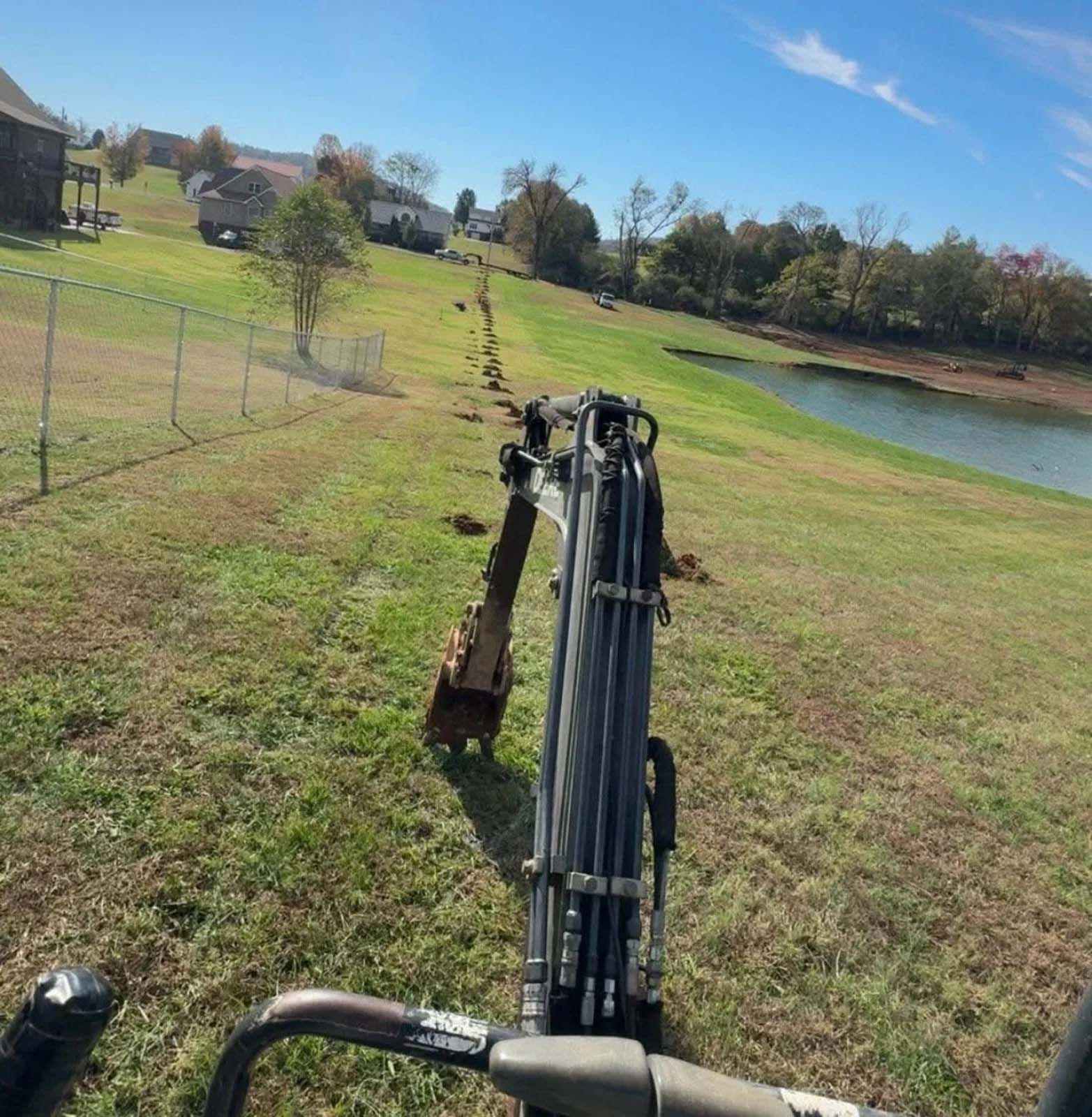 Excavator arm on a grassy slope beside a pond on a sunny day