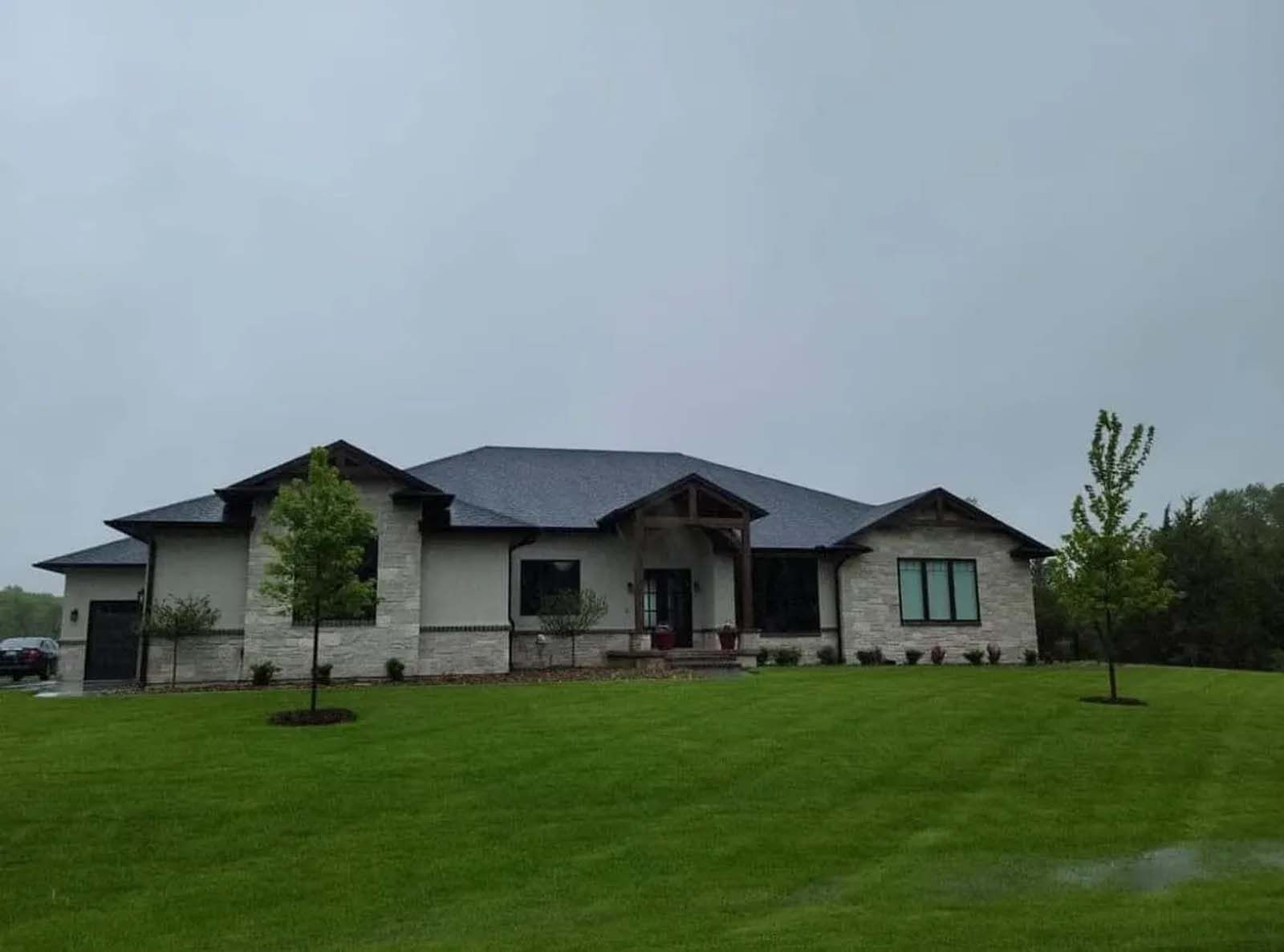 Modern stone house with dark roof on a green lawn under an overcast sky