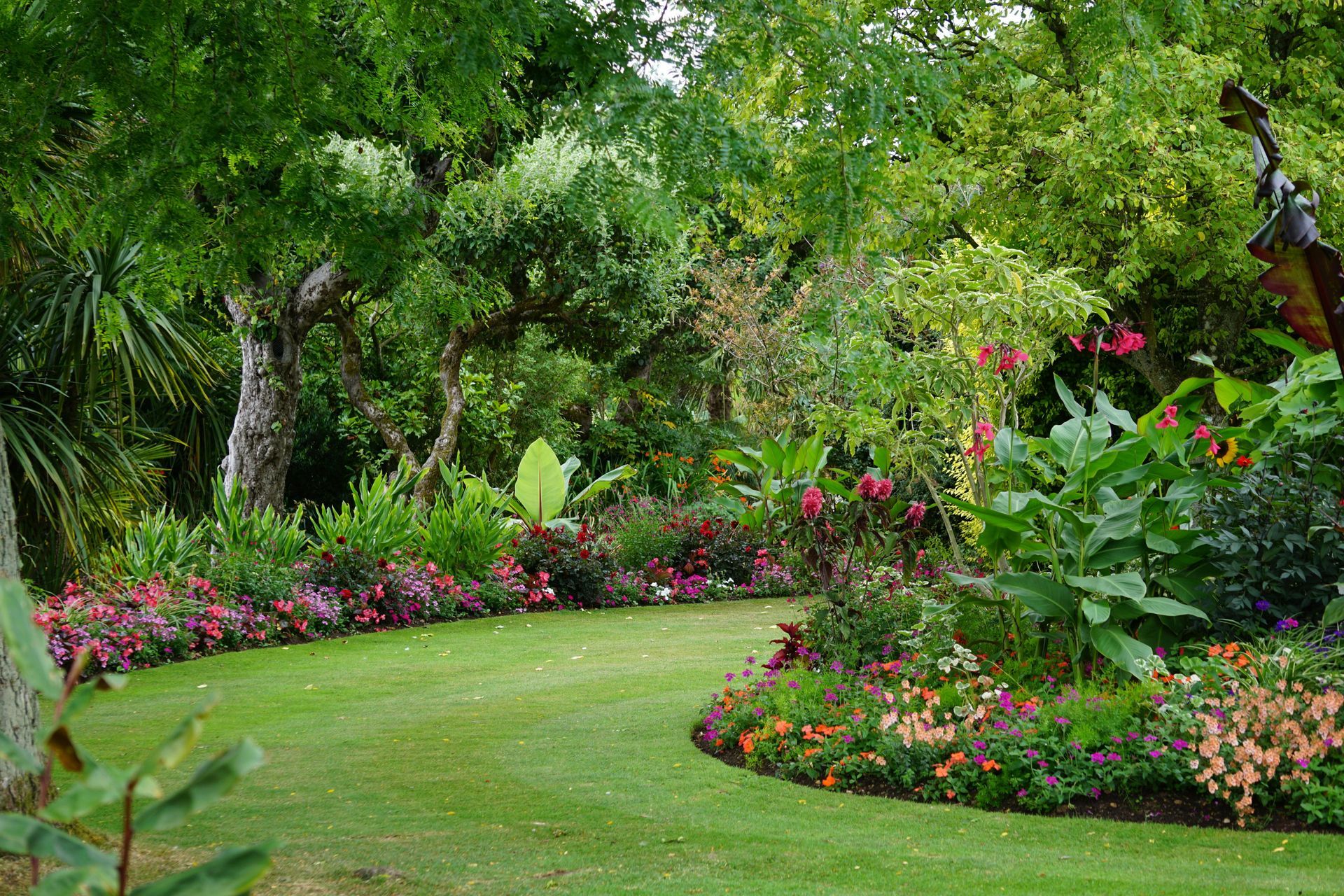 Lush garden with green lawn, trees, and colorful flower beds along a winding path