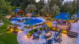 Twilight resort pool patio with blue umbrellas, lounge chairs, and warm garden lighting