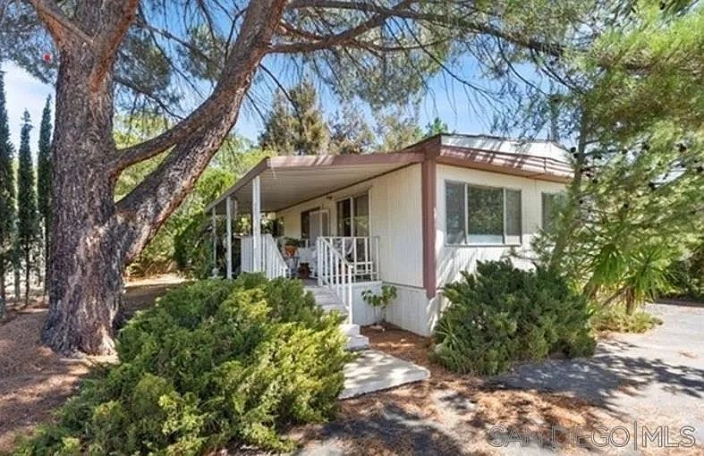 Single-story house with a covered porch, surrounded by trees and desert shrubs.
