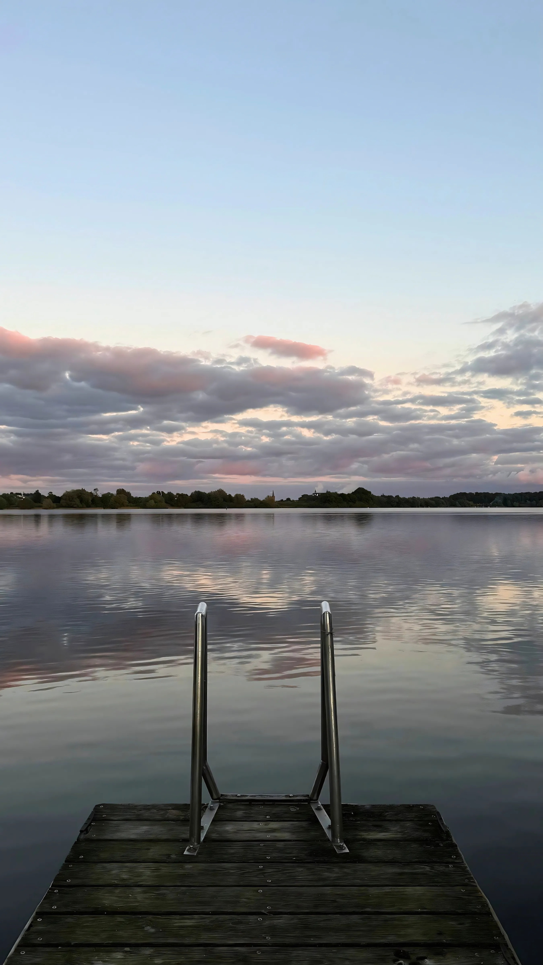 Ein Holzsteg mit einer Treppe, die bei Sonnenuntergang zu einem See führt.