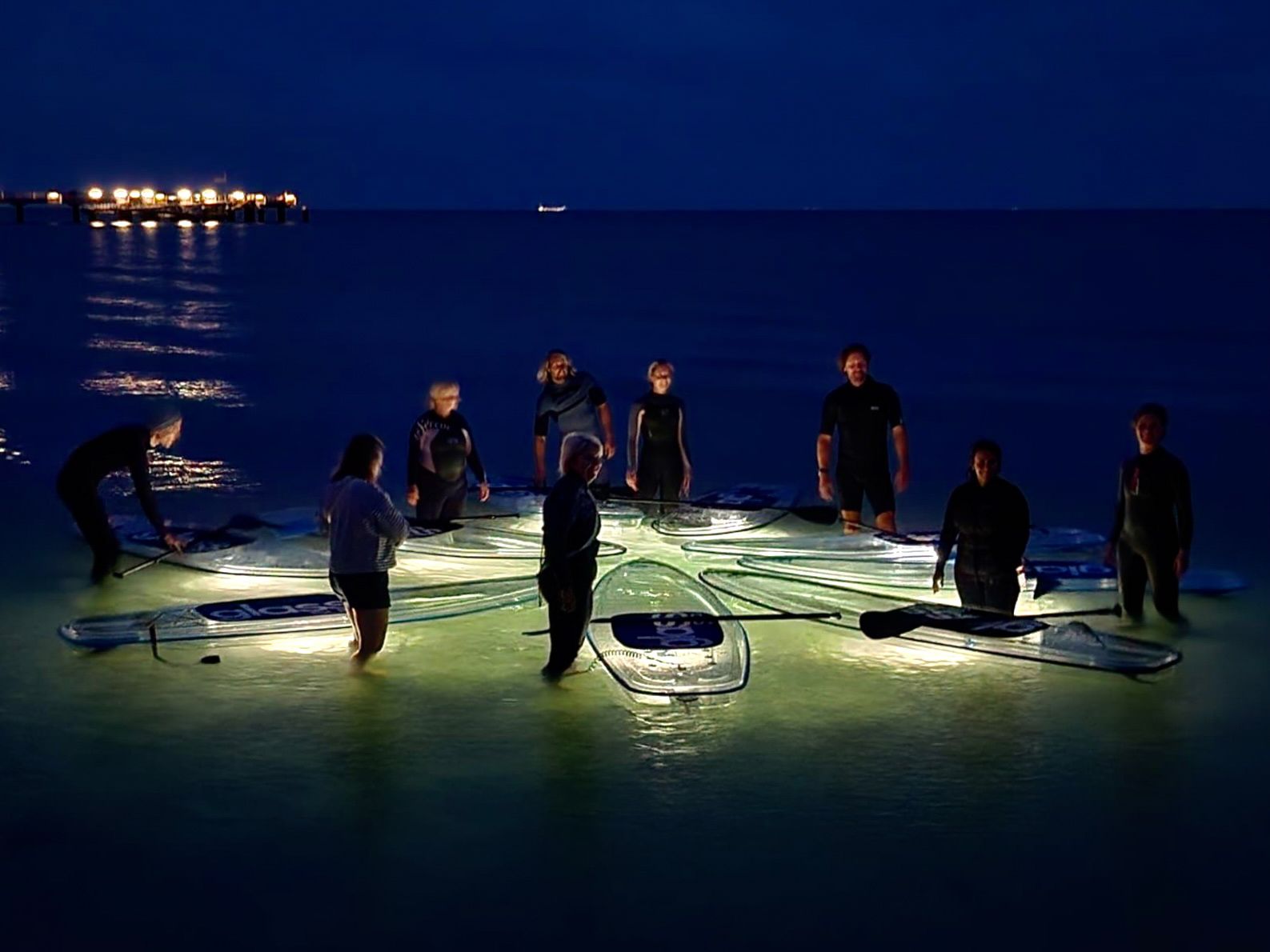 Eine Gruppe von Menschen steht nachts auf einem durchsichtigen SUP im Meer.