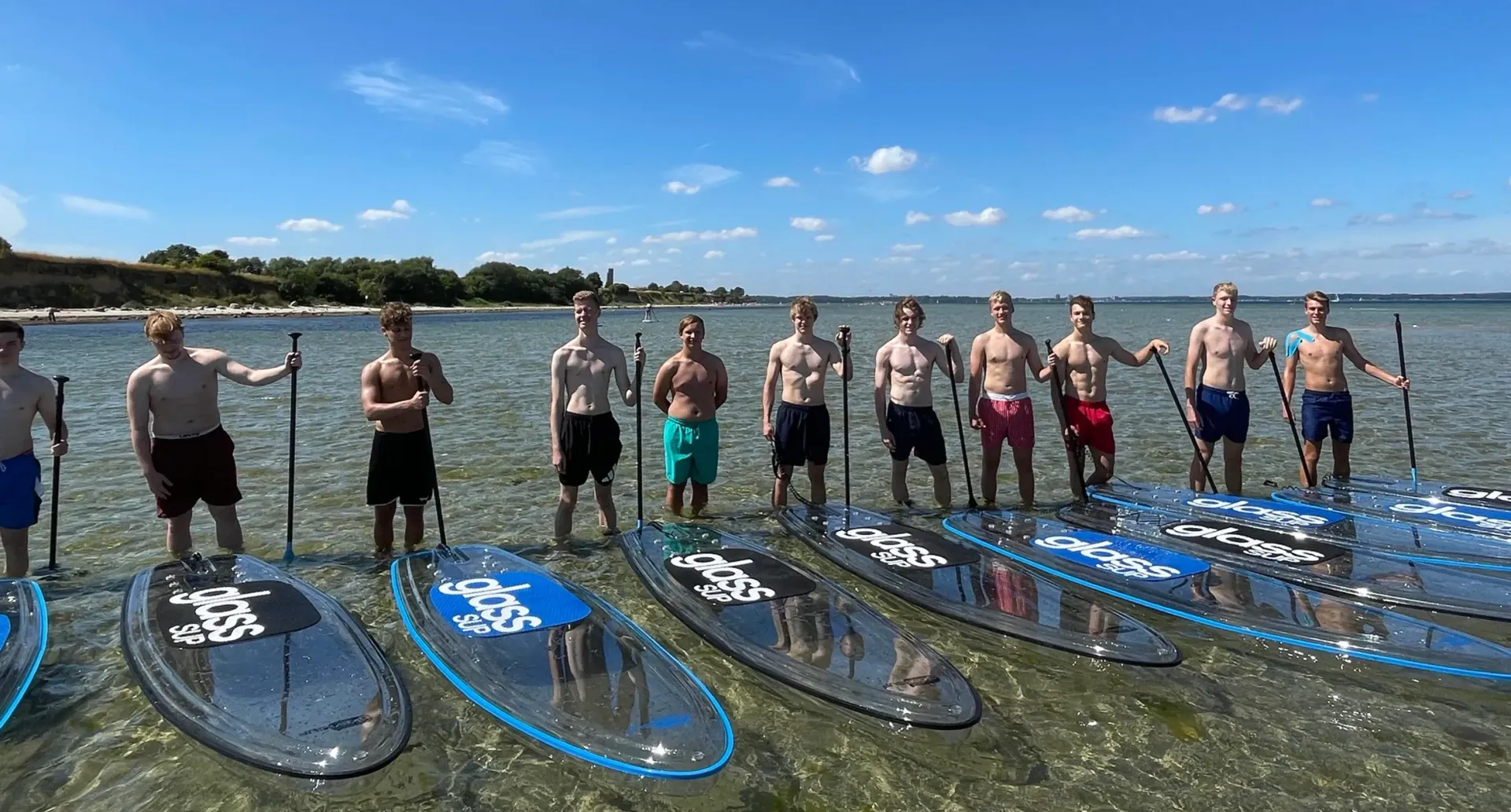 Eine Gruppe Männer steht auf durchsichtigen Paddelbrettern im Wasser.