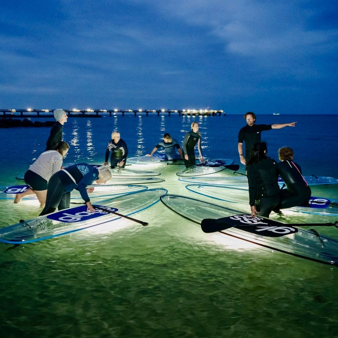 Eine Gruppe von Menschen sitzt auf durchsichtigen Surfbrettern im Wasser