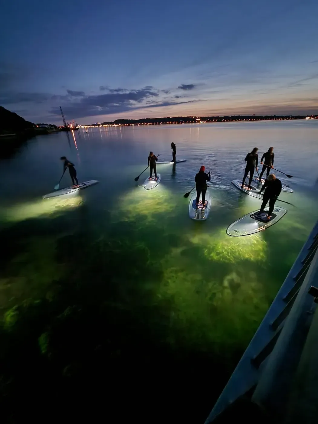 Eine Gruppe von Leuten ist nachts auf glassSups im Wasser unterwegs.