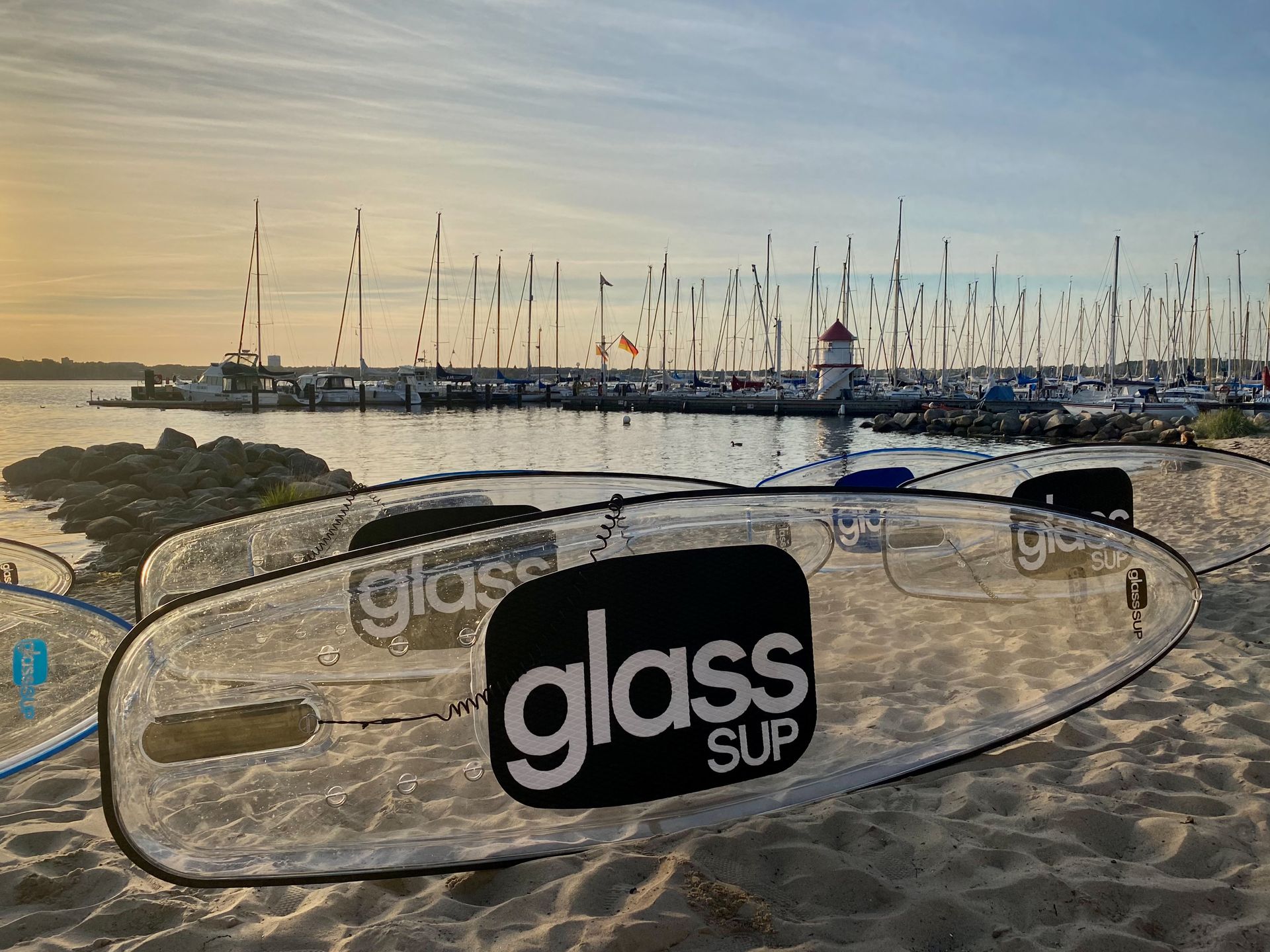 Zwei SUP-Boards aus klarem Glas liegen auf einem Sandstrand.