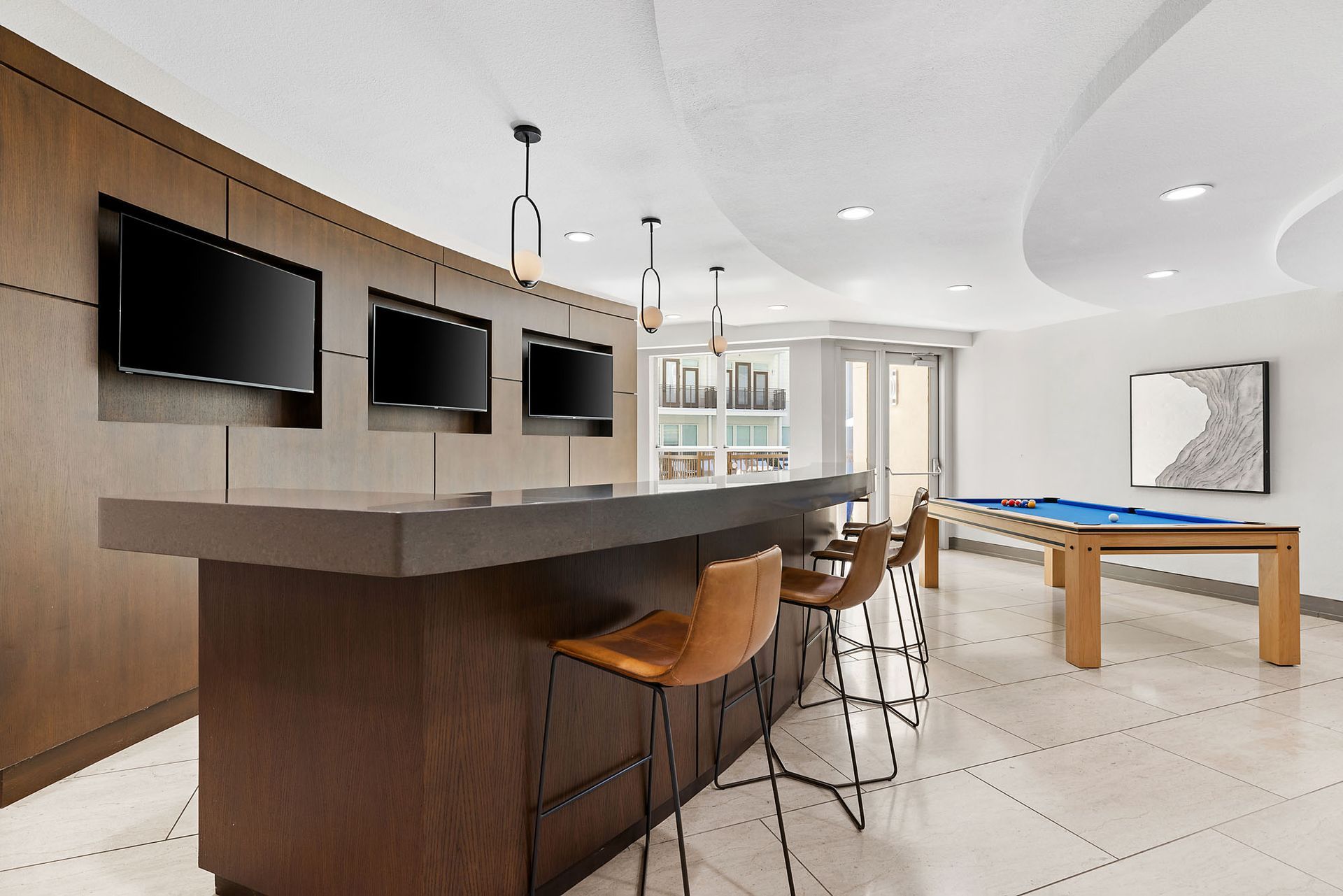 Modern game room with bar seating, multiple TVs, and a pool table in a bright, minimalist space at Marq on West 7th.