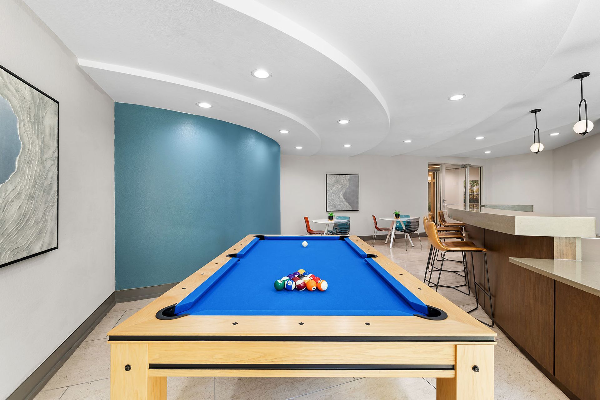 Modern basement game room with a blue pool table, bar seating, and curved ceiling lighting