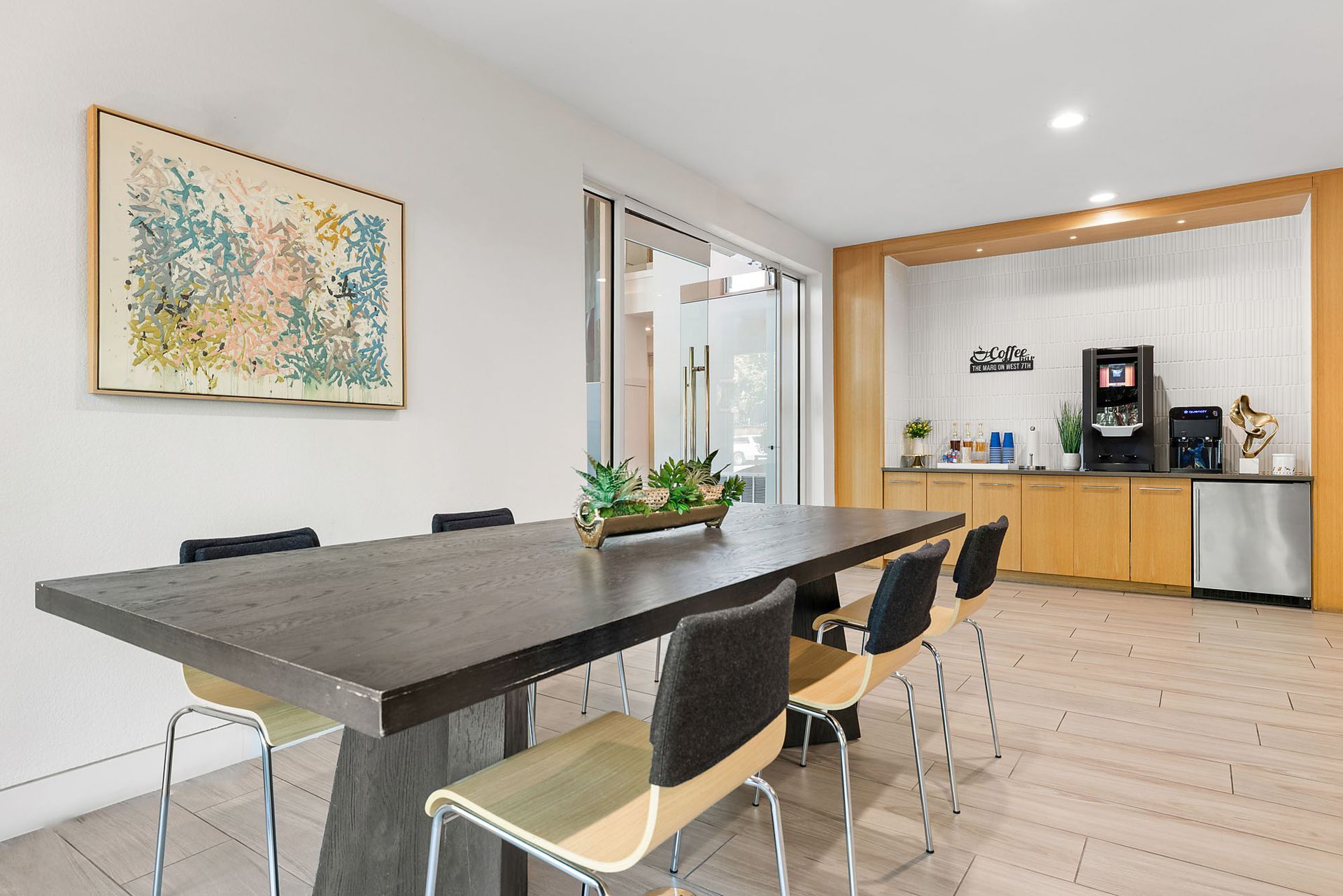 Modern conference room with long table, black chairs, wall art, and a coffee station at Marq on West 7th.