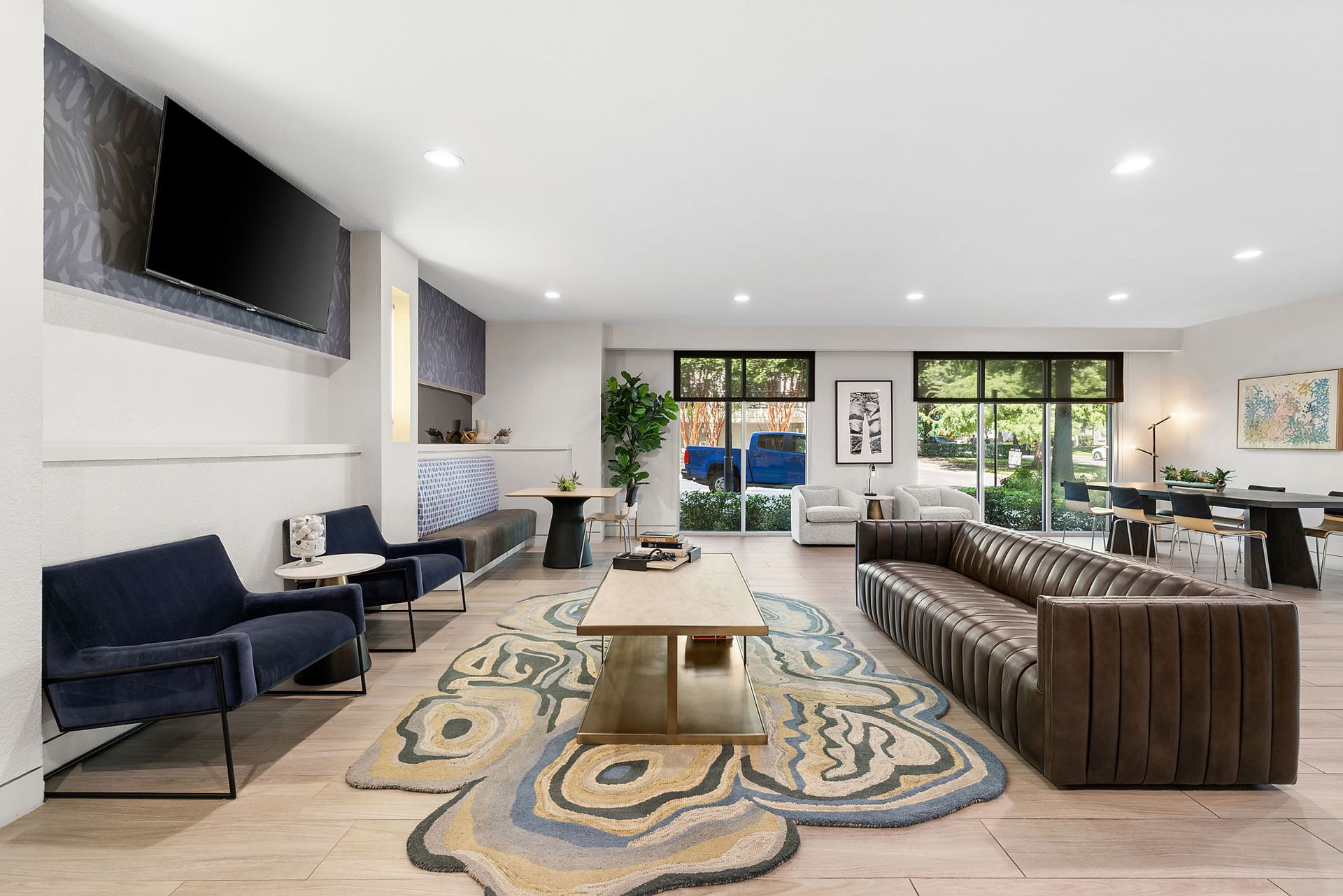Modern living room with navy and brown sofas, large wall TV, patterned rug, and bright windows at Marq on West 7th.
