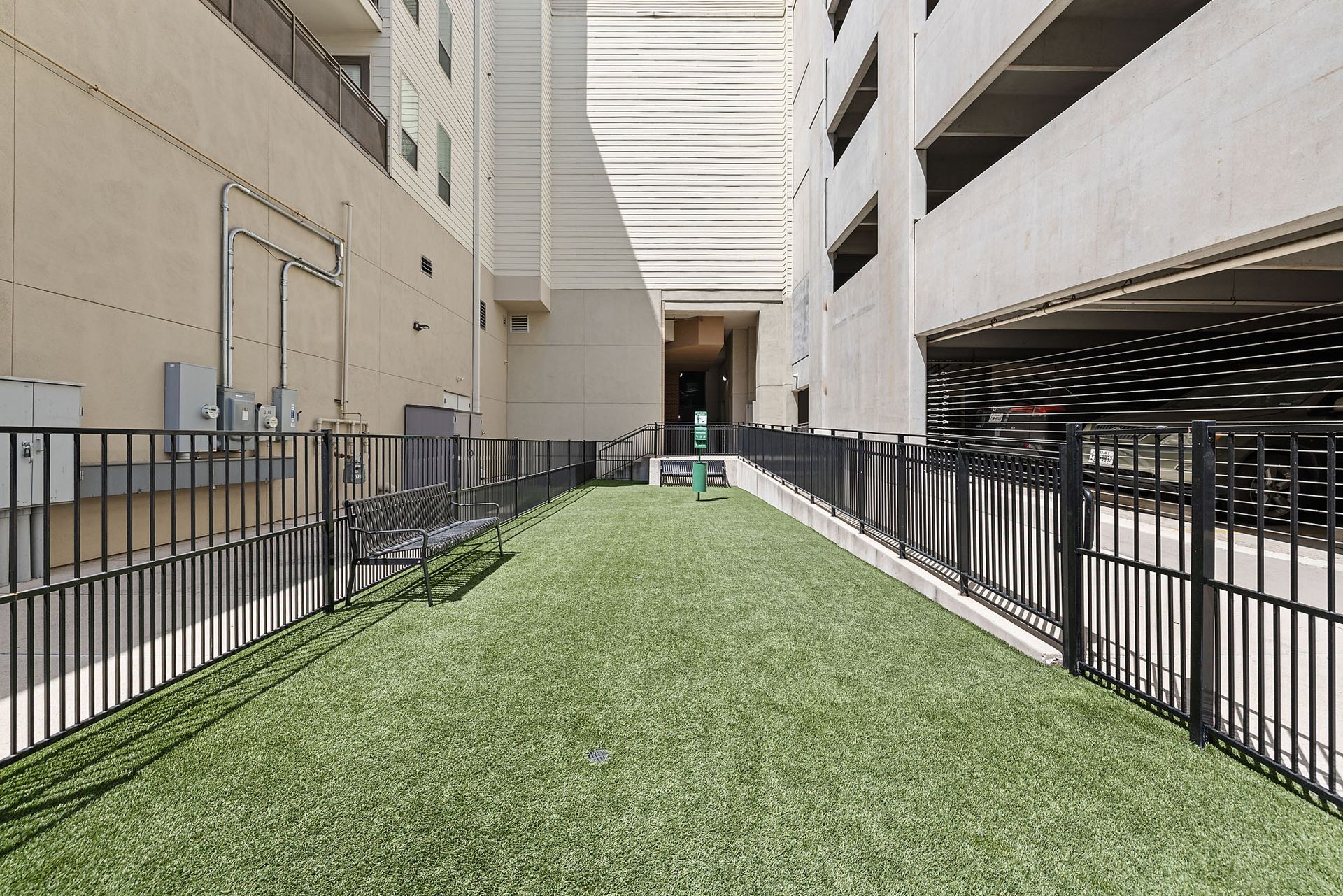 Long green rooftop walkway between beige buildings, lined with black railings and utility units at Marq on West 7th.