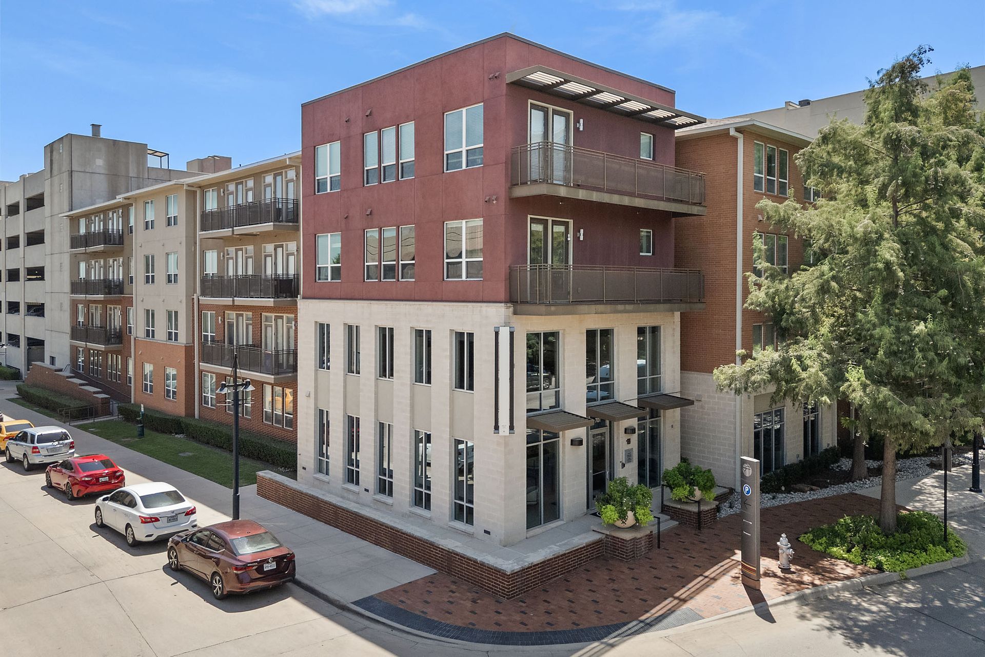 Modern red-brick apartment building on a sunny city street with parked cars and trees at Marq on West 7th.