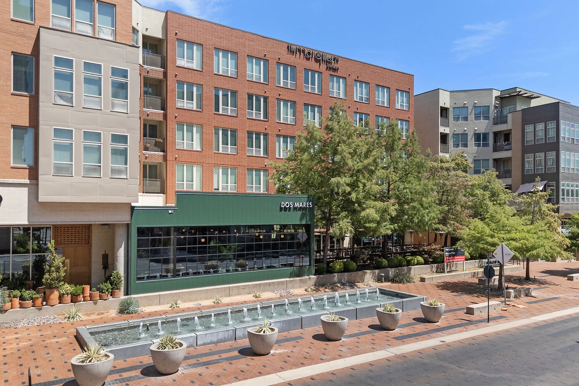 Modern apartment building with street-level shops and a small water fountain plaza in front at Marq on West 7th.