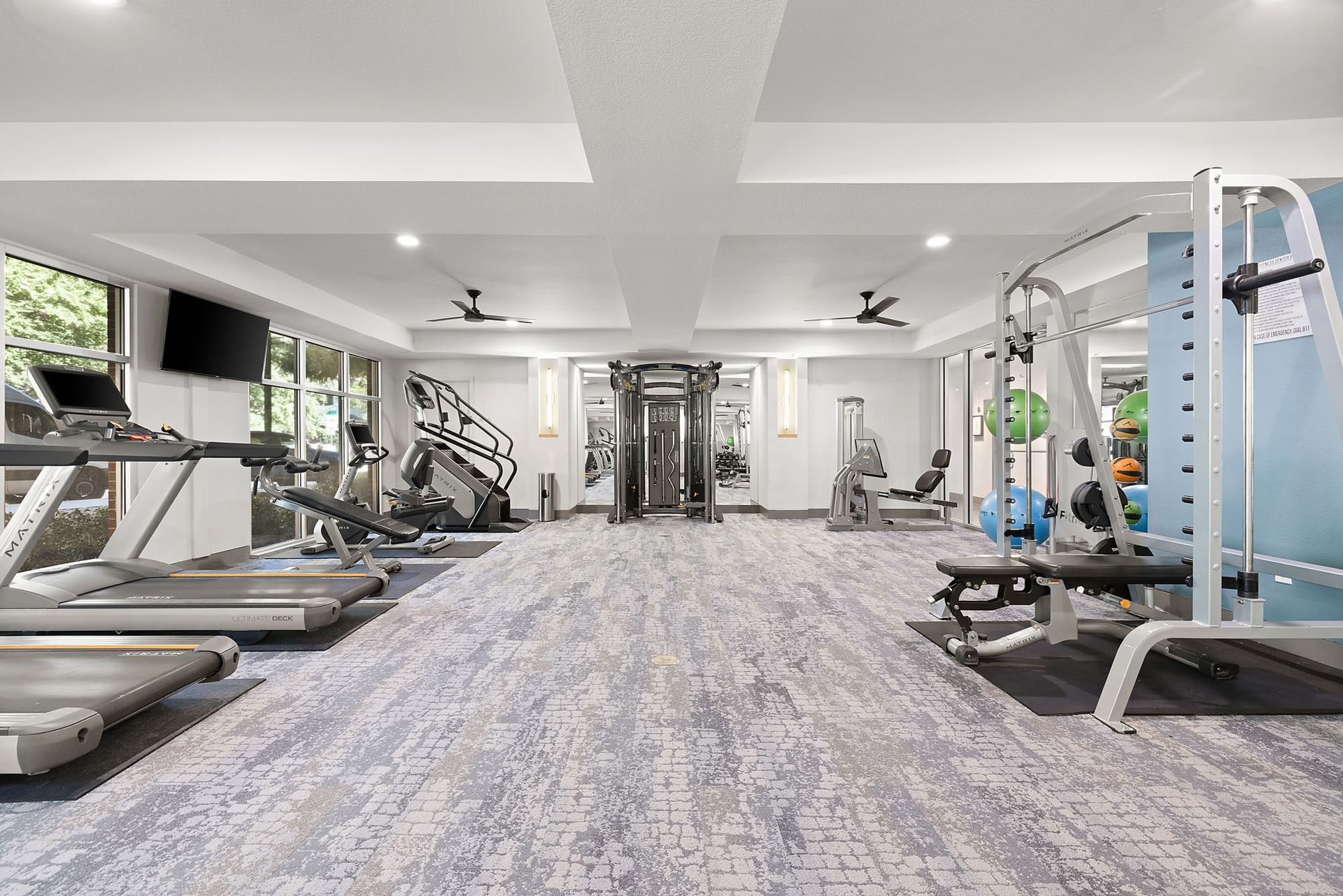 Bright modern gym with treadmills, weight machines, and a central carpeted aisle at Marq on West 7th.