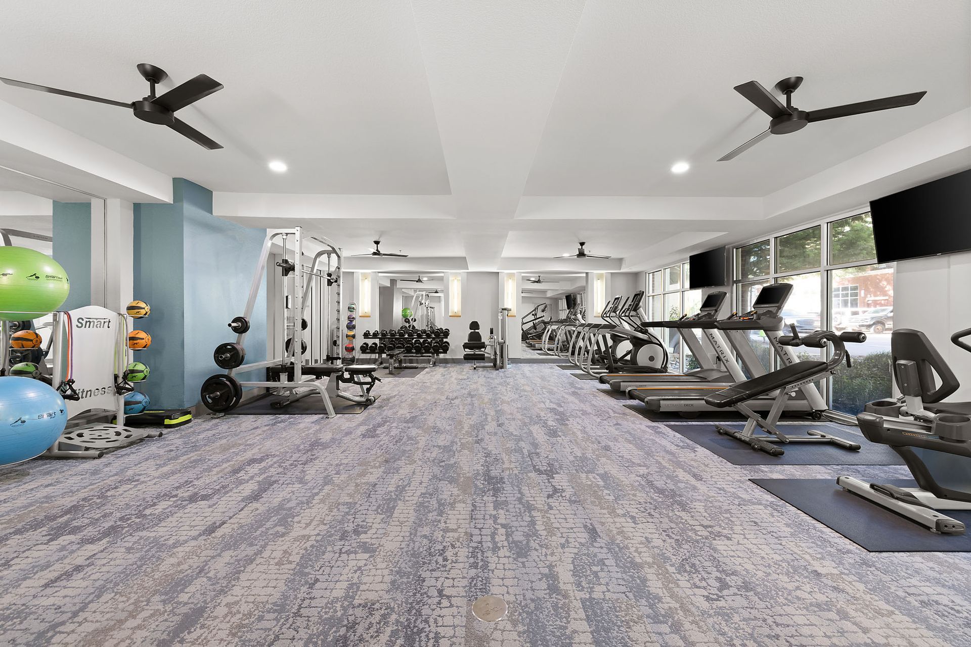 Modern gym interior with treadmills, weight machines, exercise balls, and ceiling fans at Marq on West 7th.
