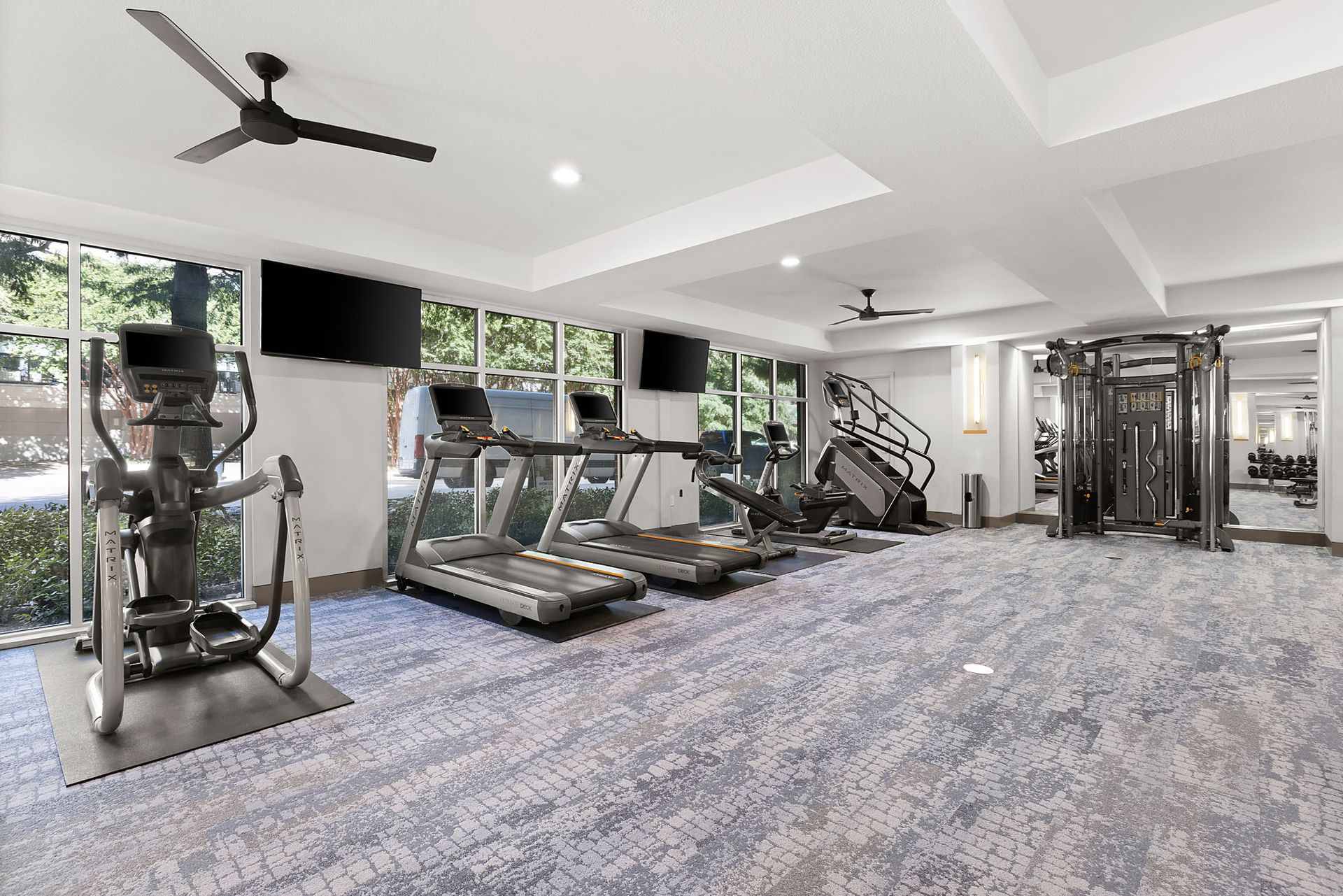 Modern gym with treadmills, weight machines, and ceiling fans in a bright, carpeted room at Marq on West 7th.