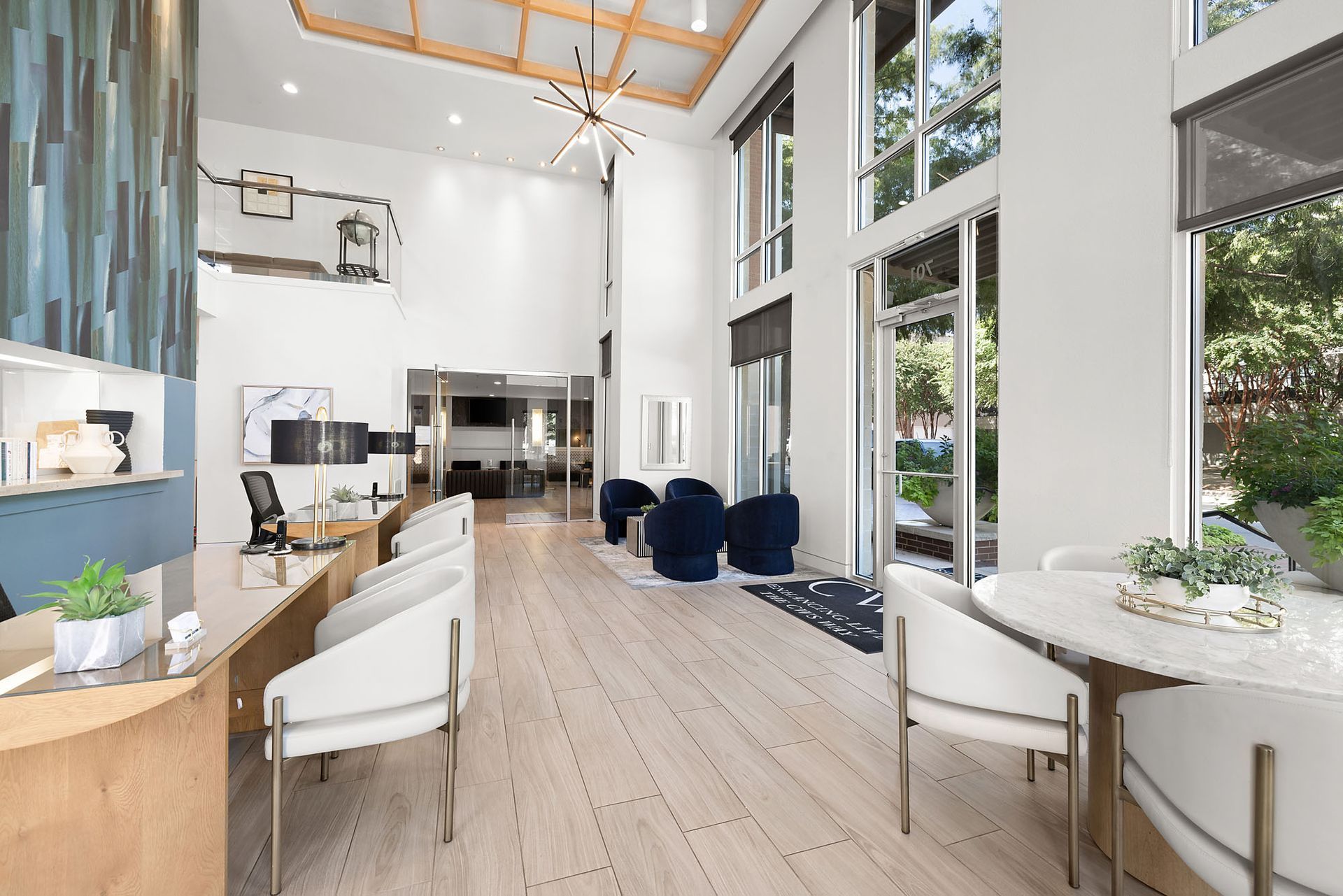 Bright modern lobby with high ceilings, white chairs, blue sofas, and large windows overlooking greenery at Marq on West 7th.
