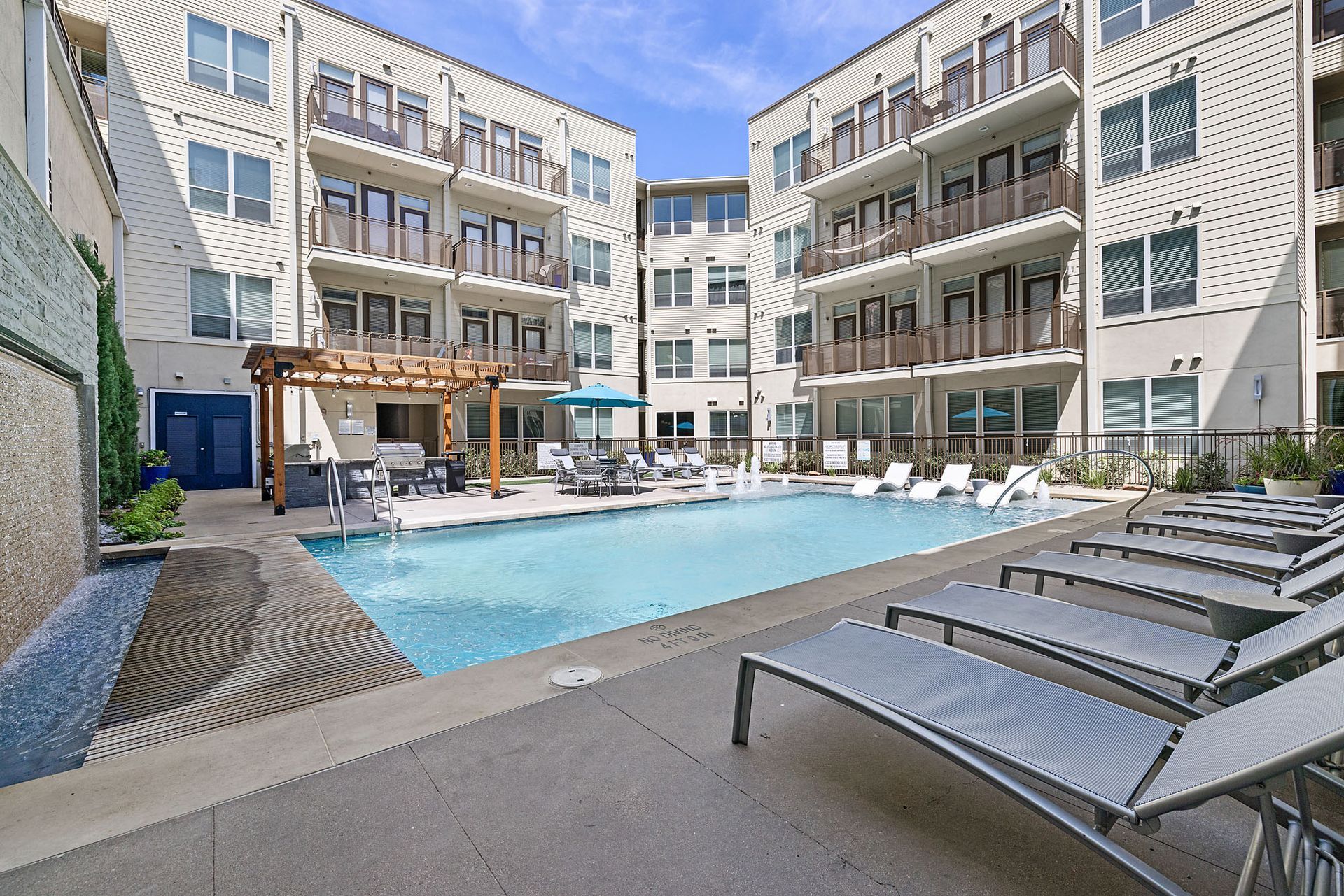 Modern apartment courtyard with a swimming pool and lounge chairs under a clear blue sky at Marq on West 7th.