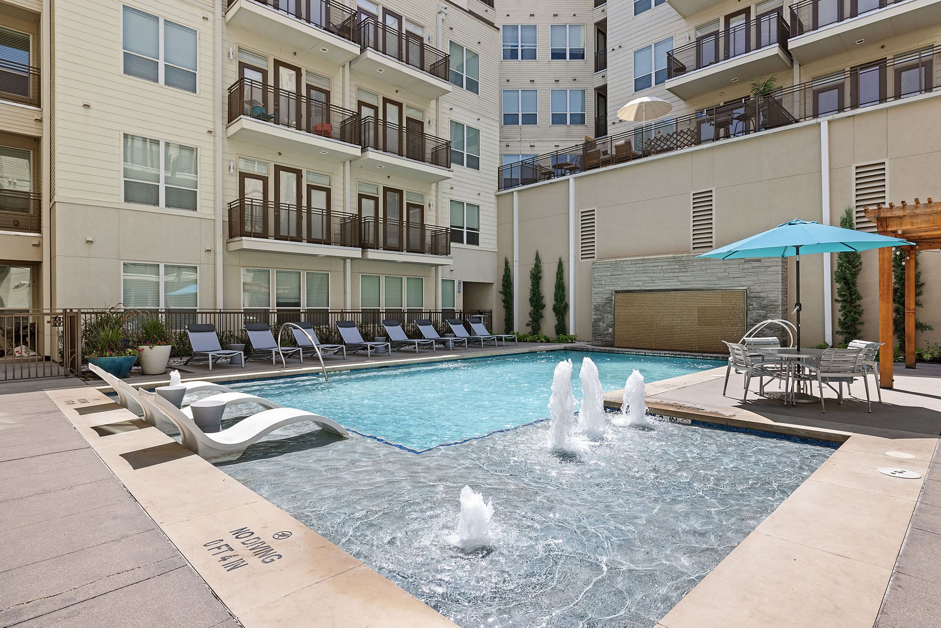 Apartment courtyard pool with lounge chairs, umbrellas, and water fountains at Marq on West 7th.