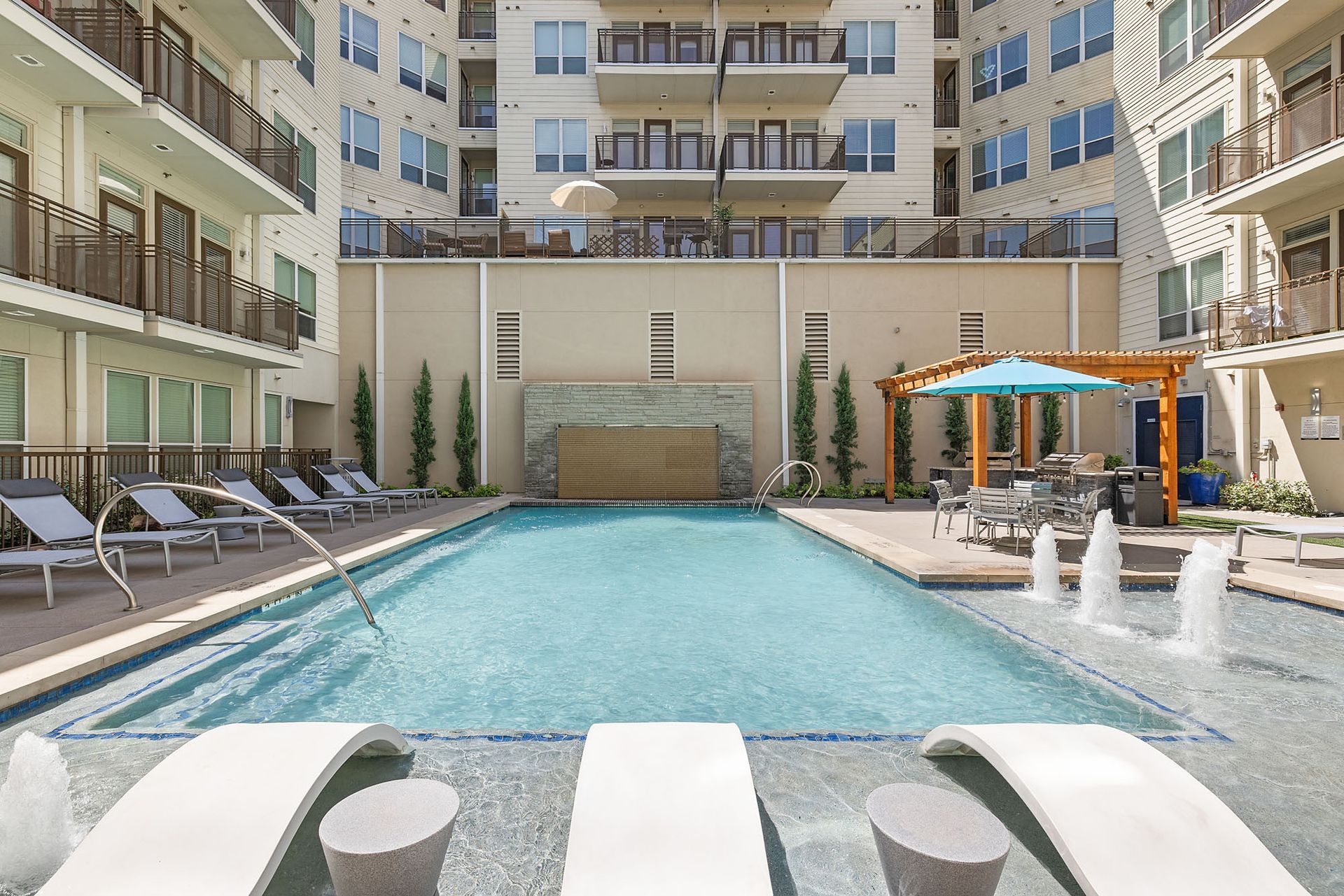 Courtyard pool surrounded by lounge chairs in a modern apartment complex