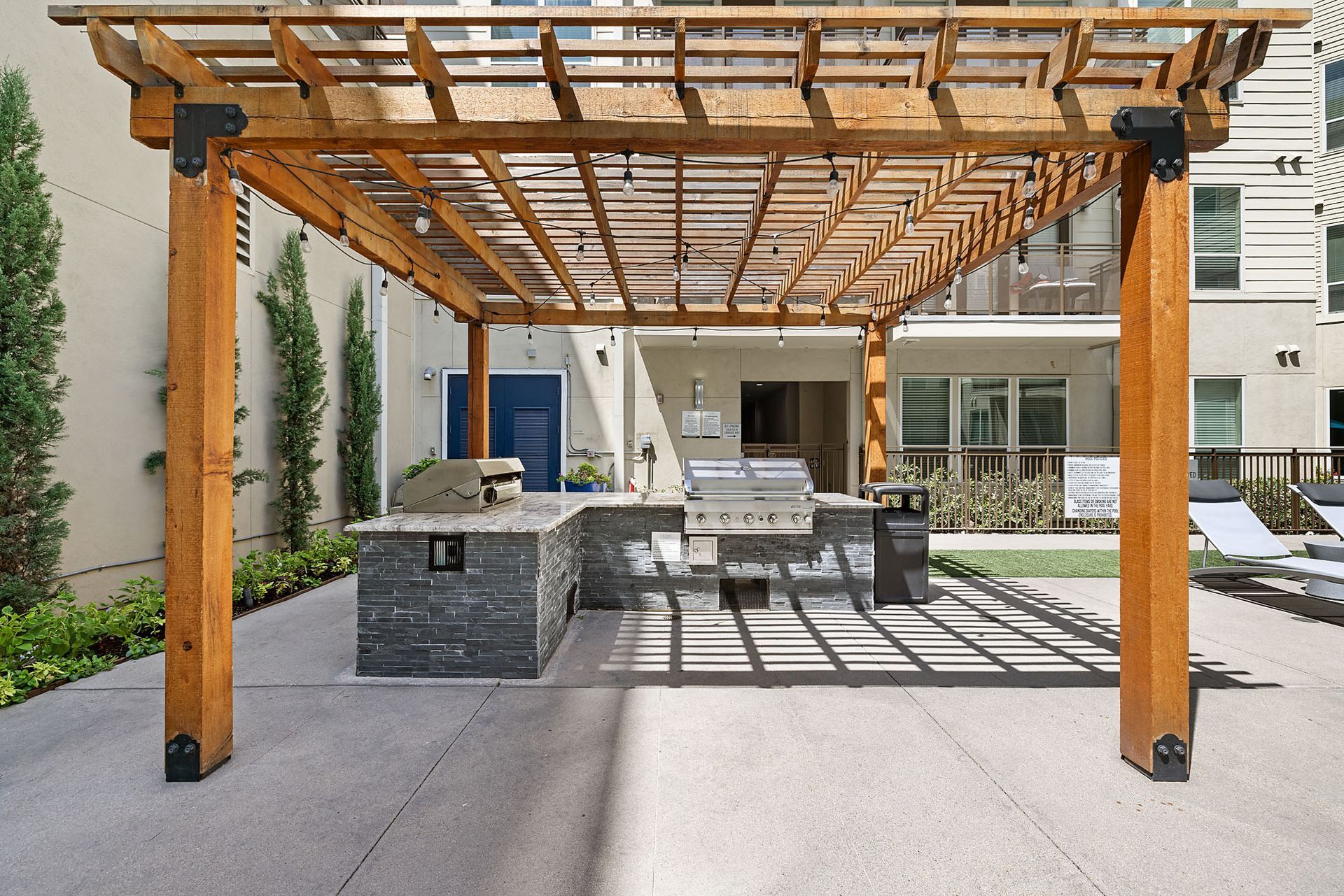 Outdoor patio with wooden pergola, gray seating, and a dining table in a modern courtyard