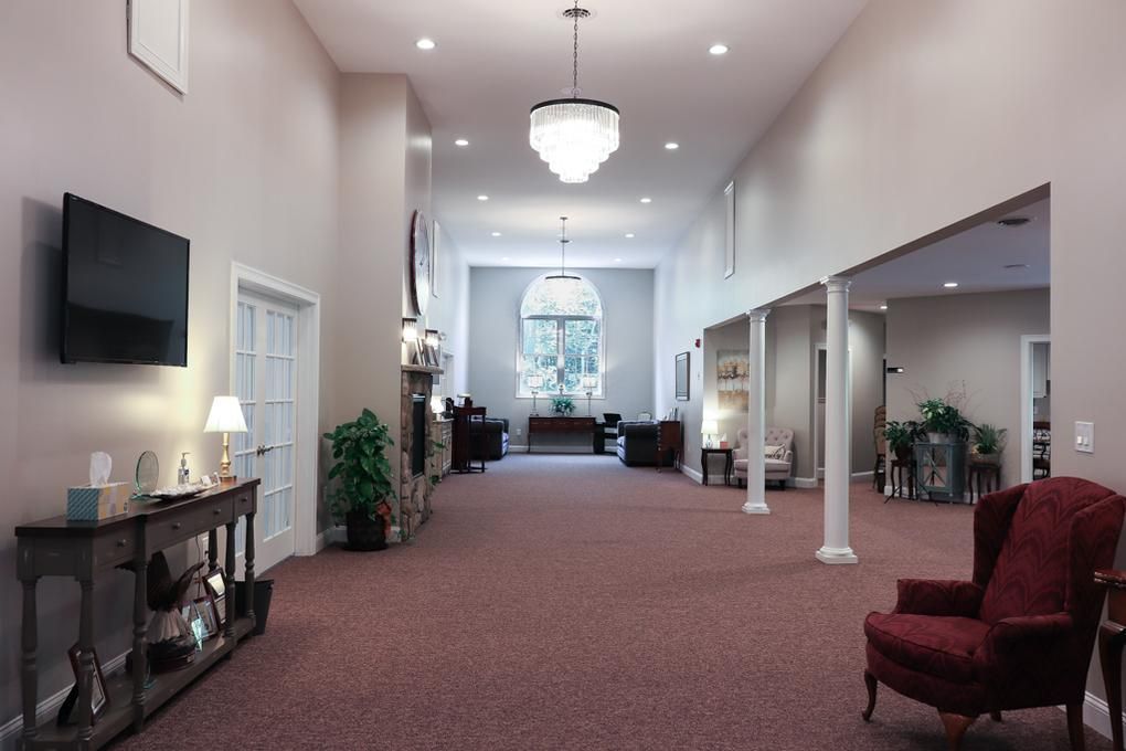 Bright church hallway with maroon carpet, white columns, chairs, and wall-mounted TV