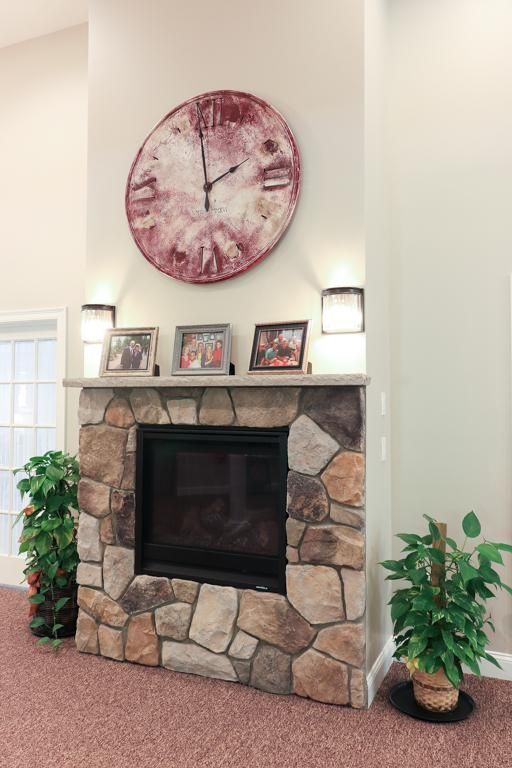 Stone fireplace with framed photos, a large wall clock, and potted plants in a living room.
