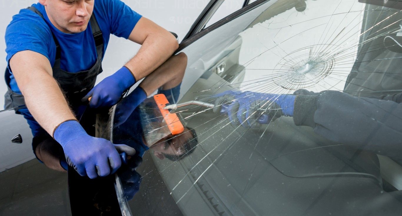 Person in blue gloves uses a squeegee to clean a cracked car windshield