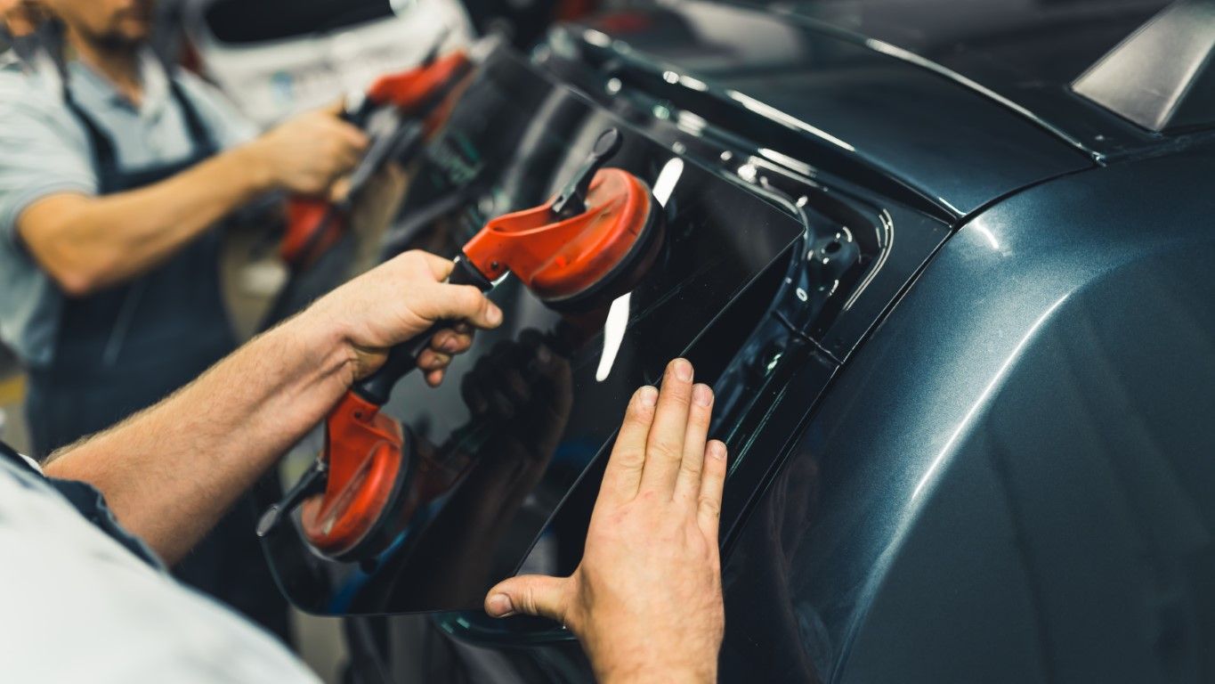 Hands using suction cups to install or remove a car window or panel in a garage.
