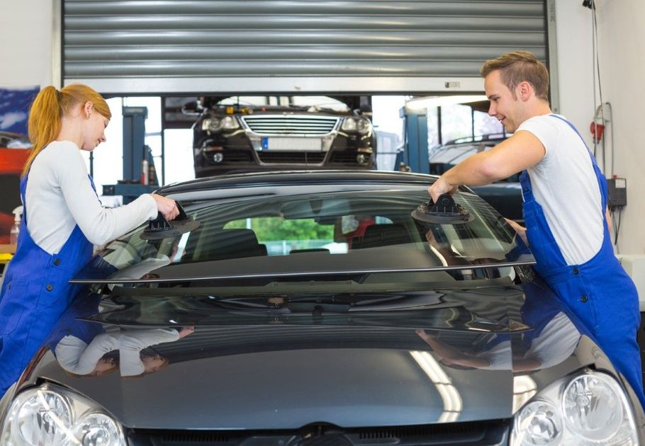 Two mechanics in blue overalls working on a black car in a garage