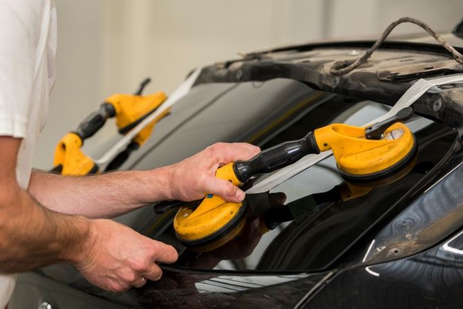 Technician using a yellow suction lifter to repair a cracked car windshield