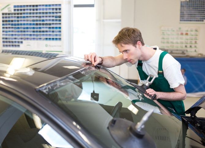 Mechanic in green overalls inspecting a car windshield in a workshop