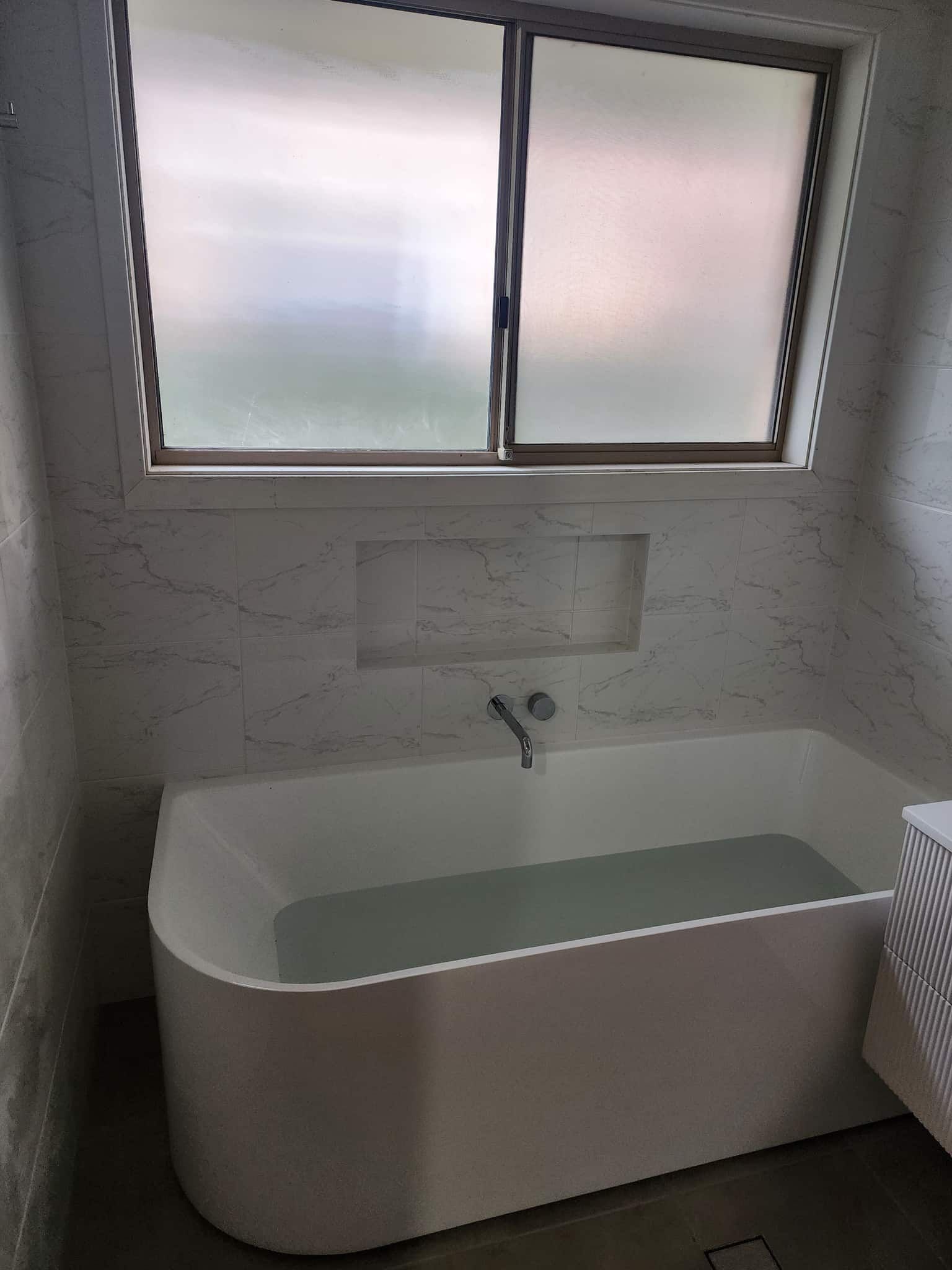 A Bathtub Is Filled With Water In A Bathroom Next To A Window — Renovate A Space In Woy Woy, NSW