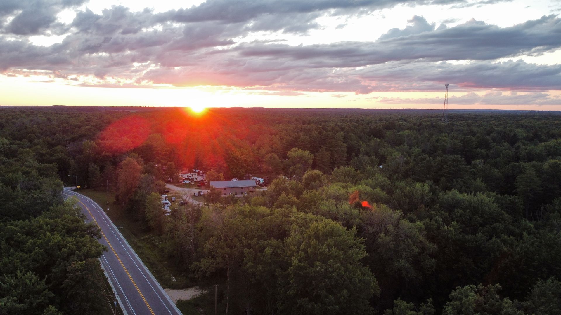 An aerial view of a road going through a forest at sunset.