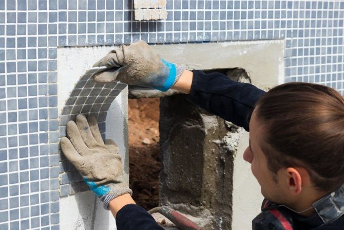 Worker installing gray tile around a window opening on an exterior wall