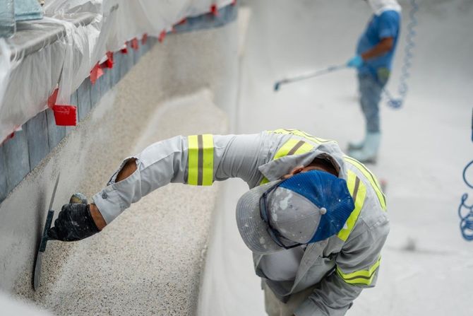 Worker in reflective vest and hard hat applying coating to a concrete wall on a construction site