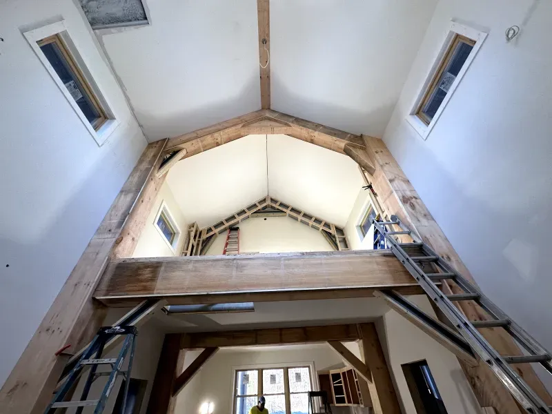 Interior view of a high ceiling with exposed wood beams, skylights, and a ladder during renovation
