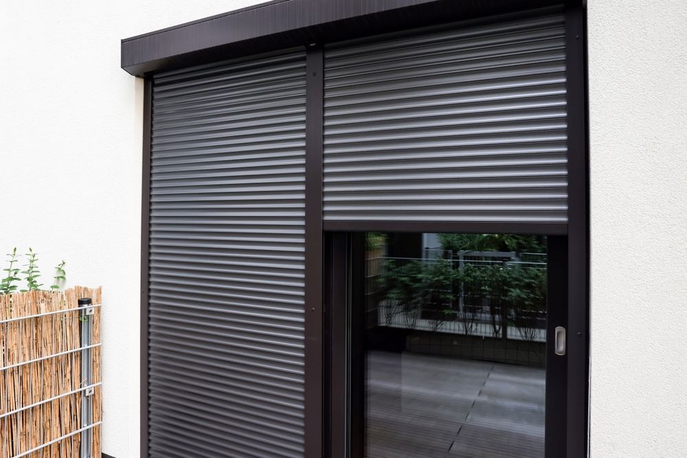 A Sliding Glass Door With A Black Roller Shutter On It — Maxview Blinds and Shutters in Beresfield, NSW