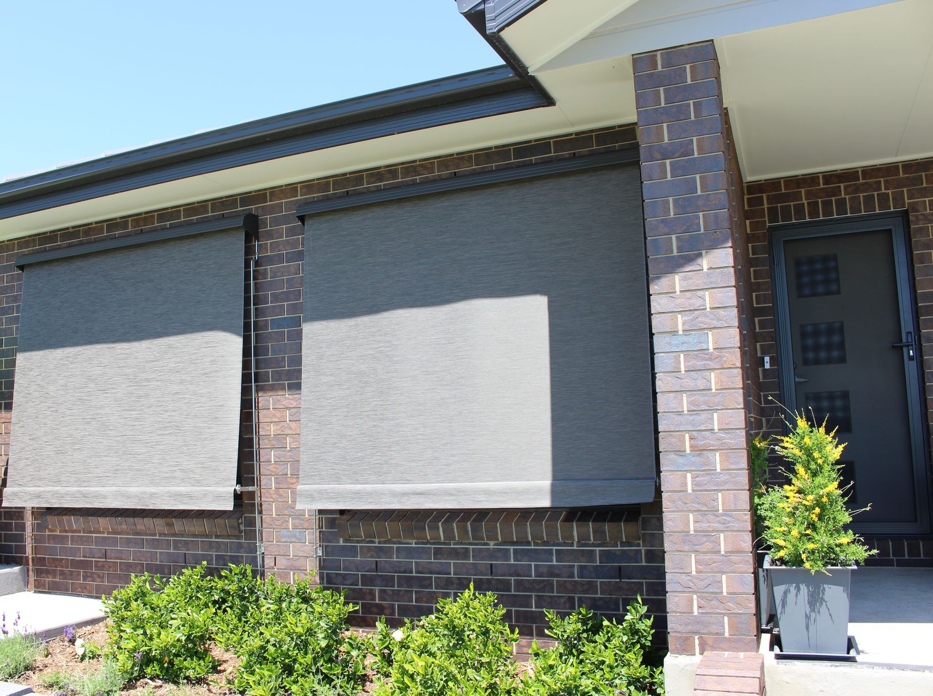 Modern brick house with outdoor blinds, dark door, garden — Maxview Blinds and Shutters in Beresfield, NSW