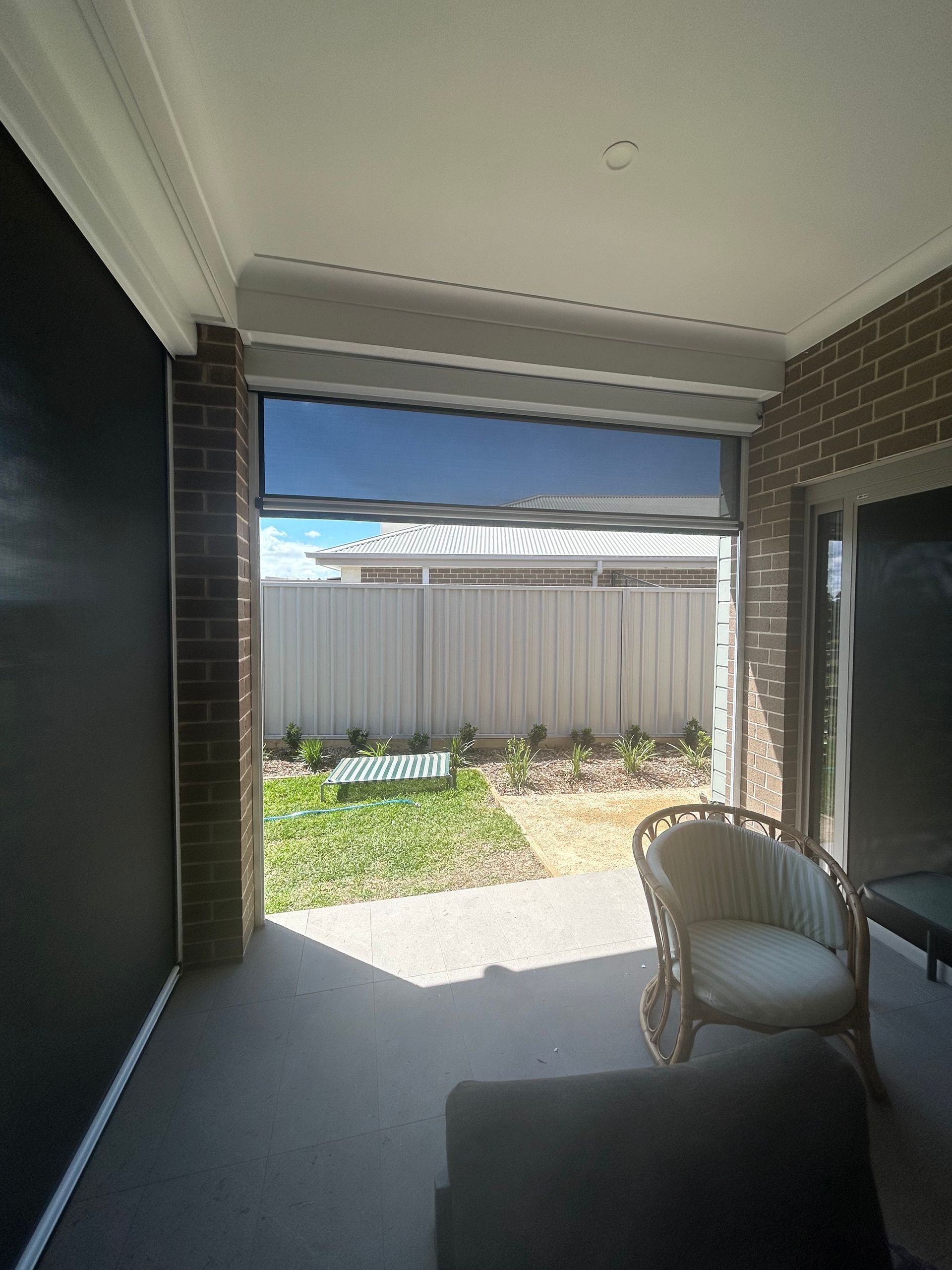Covered patio with Ziptrak blind, wicker chair, and view of a small backyard — Maxview Blinds and Shutters in Beresfield, NSW