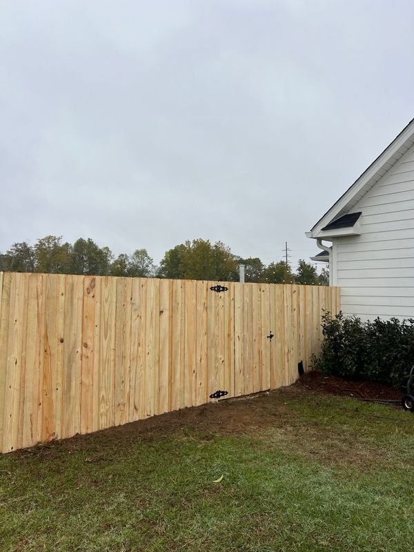 Wooden privacy fence beside a white house under a cloudy sky.