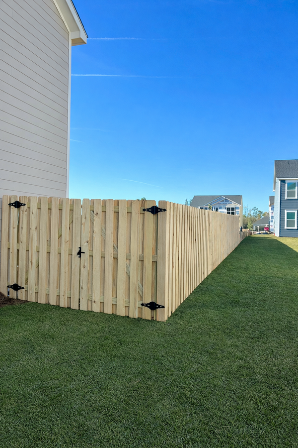 Wooden privacy fence along a grassy yard beside a white house under a blue sky