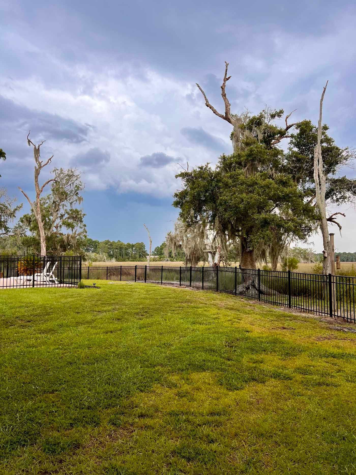 A large lush green field with a fence and trees in the background.
