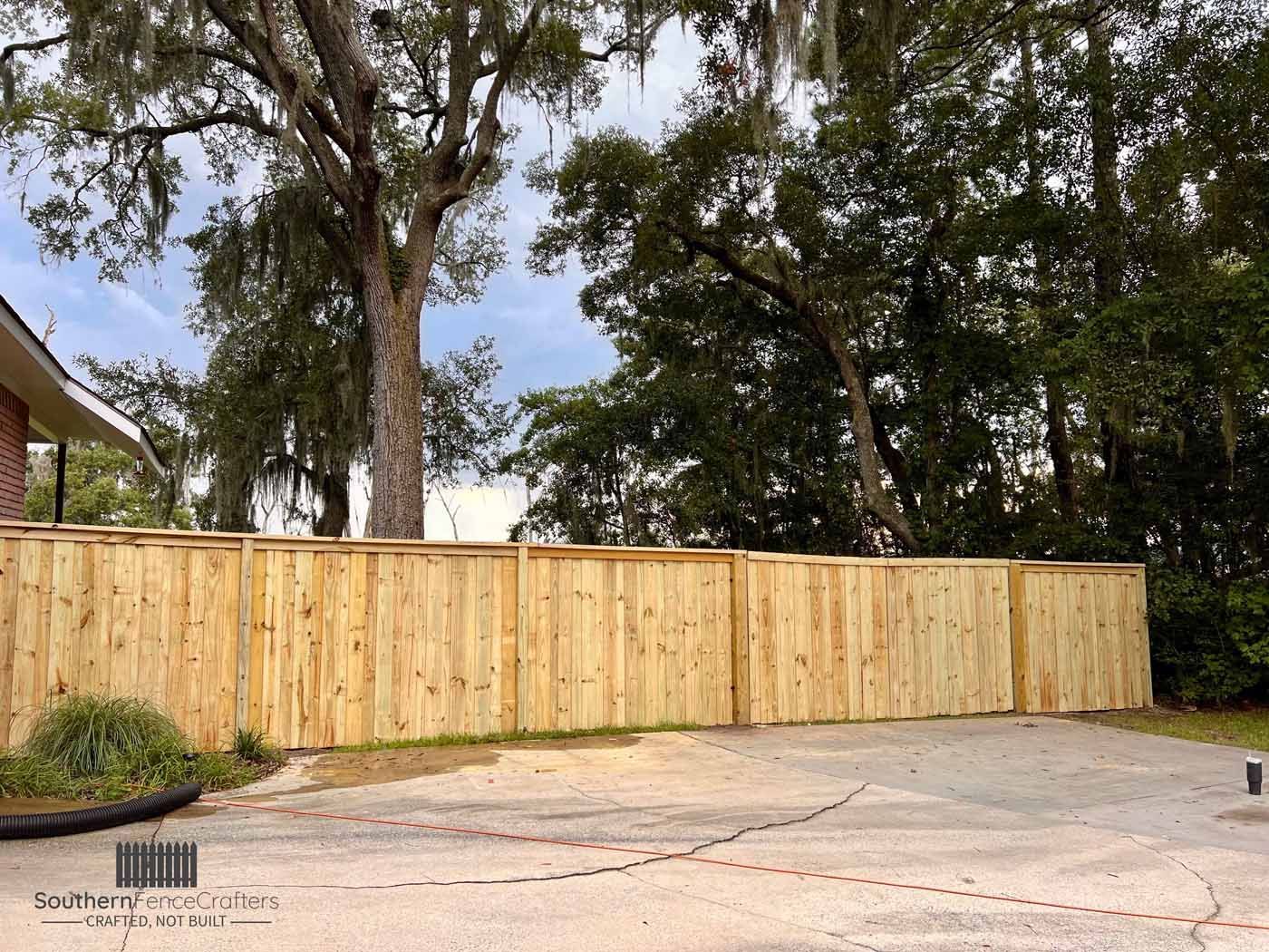 A wooden fence surrounds a driveway with trees in the background.