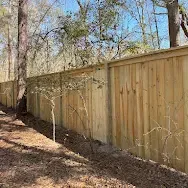 Wooden privacy fence along a wooded yard with fallen leaves and bare trees