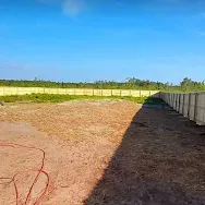Open dirt lot beside a concrete wall under a bright blue sky